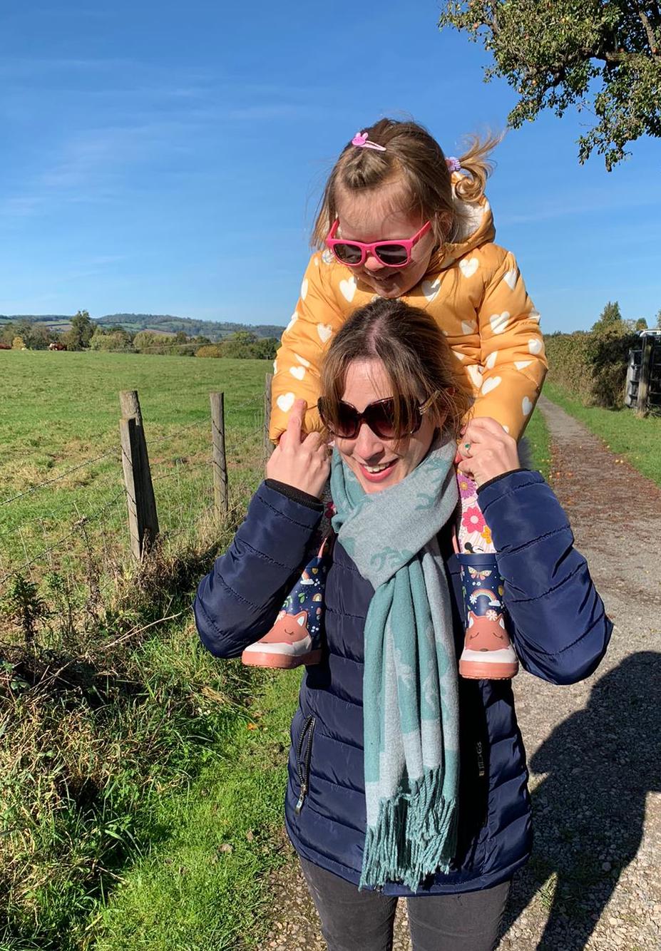 Emma Gorton-Garlick laughing during a countryside walk, with her daughter Layla on her shoulders, enjoying nature and family time.