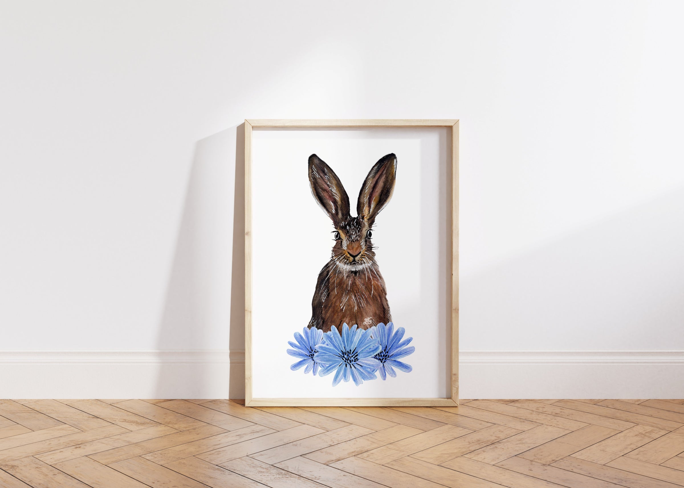 image of a framed print of a hare and some blue chicory flowers against plain background on wooden floor. perfect for mother's day gift. 