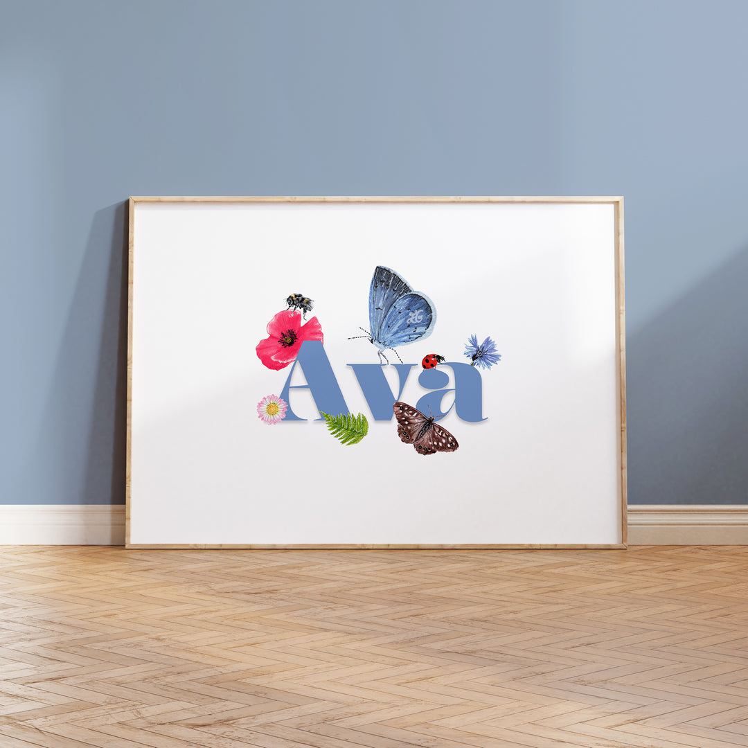 Personalised wildlife meadow name print with "Ava" in soft blue, framed on a wooden floor against a painted blue wall, featuring UK meadow flowers and insects.