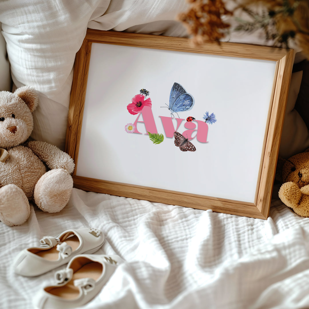 Personalised wildlife meadow name print with "Ava" in soft pink, framed on a fabric background, featuring UK meadow flowers and insects.