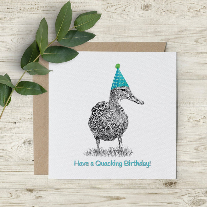 Hand-drawn charcoal sketch of a duck wearing a green watercolour party hat, with the words "Have a Quacking Birthday!" on a cutaway edge card.