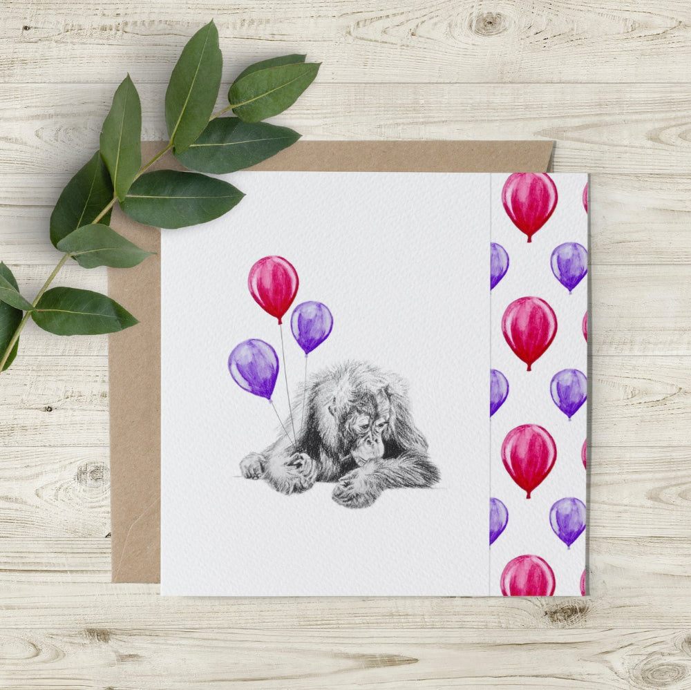 Eco-friendly Happy Birthday card featuring a hand-drawn baby orangutan with pink and purple balloons and a unique cutaway edge.