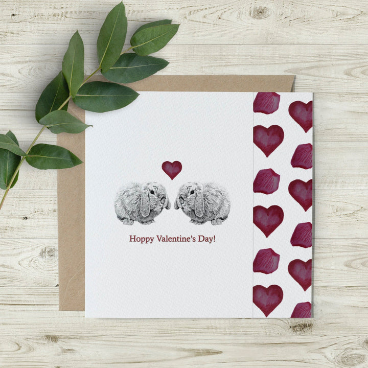 Eco-friendly Hoppy Valentine’s Day card featuring hand-drawn lop-eared bunnies, red watercolour hearts, and a cutaway edge. Made in the UK and sustainably printed.