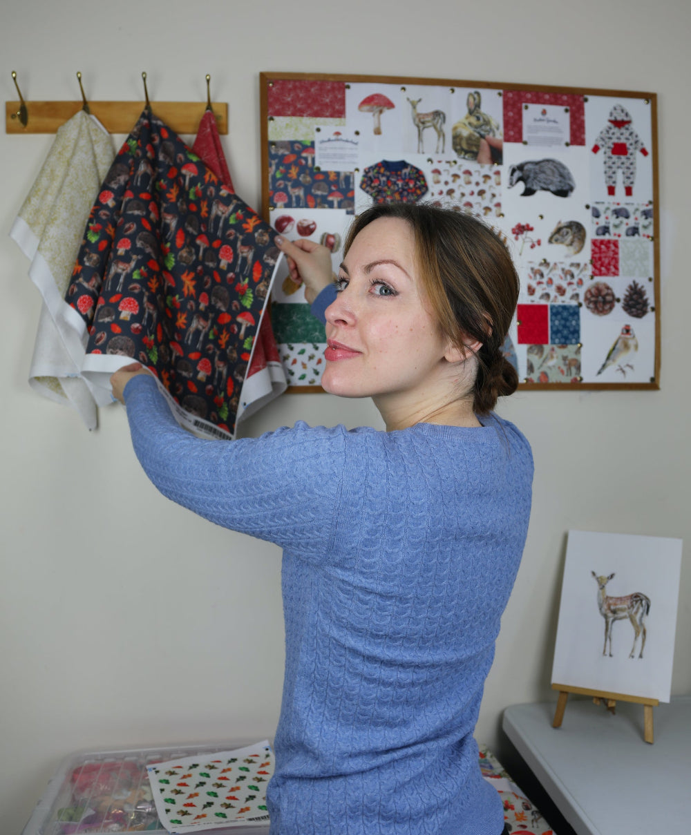 Emma standing beside her design inspiration board filled with animal and wildlife sketches, showcasing her nature-inspired printed fabric—perfect for licensed product design and brand collaborations