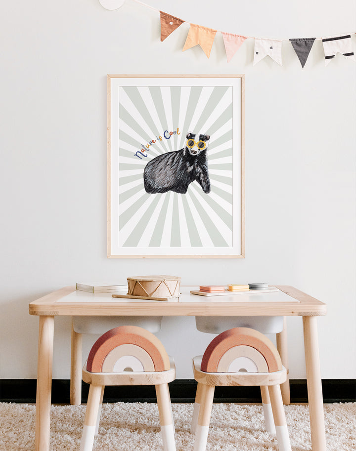 "nature is cool" art print framed and on wall of child's playroom desk. The print is of a badger against a green starburst.