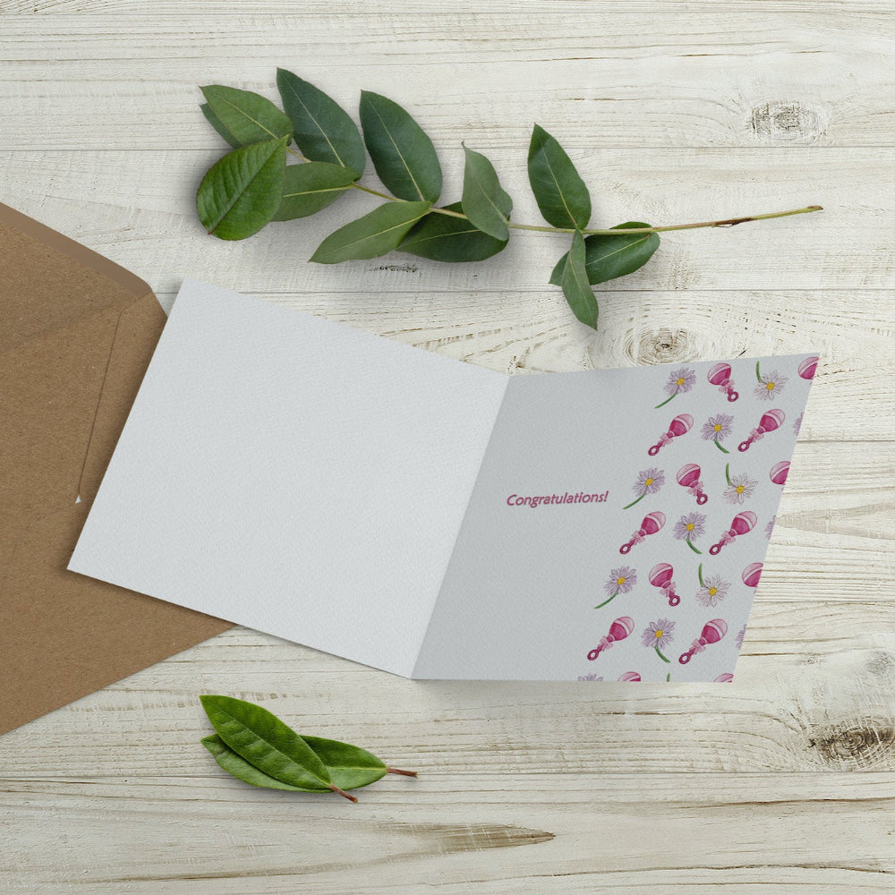 Inside of new baby girl card, featuring a pink watercolour flower and rattle design with a “Congratulations” message. Printed on sustainable paper, supporting wildlife charities.