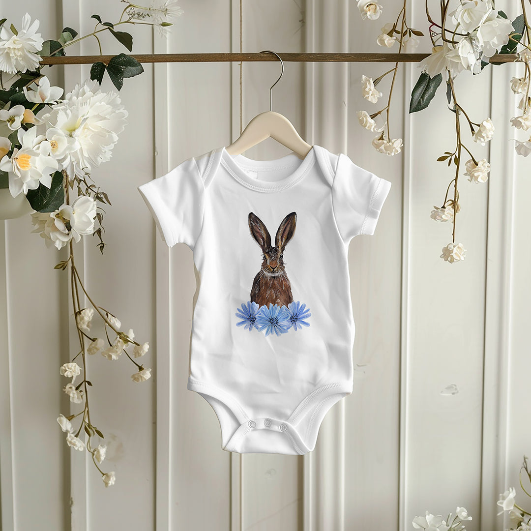 Baby girl wearing hare and chicory bodysuit, lying on a soft blanket with white headband