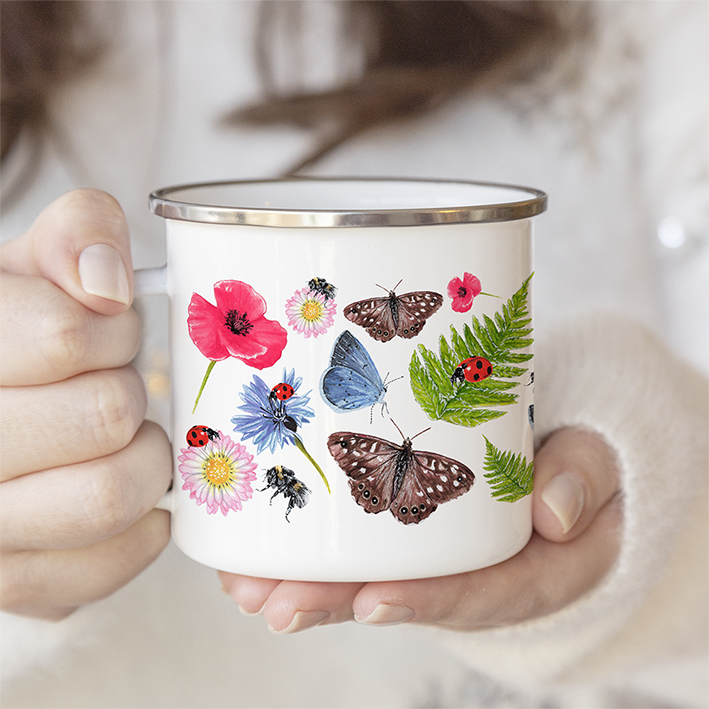 Close-up of a woman’s hand holding the Summer Meadow enamel mug, showing butterfly and wildflower design