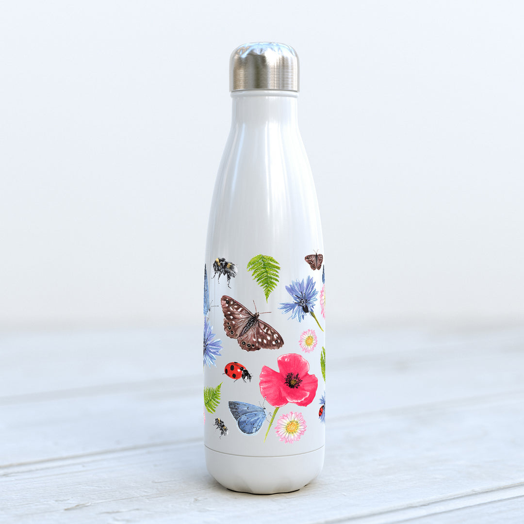 Summer Meadow insulated bottle pictured on a pale grey wooden surface, showing butterflies, bees, and wildflowers pattern