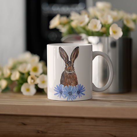Hare and chicory ceramic mug on a wooden kitchen surface with flowers in the background.